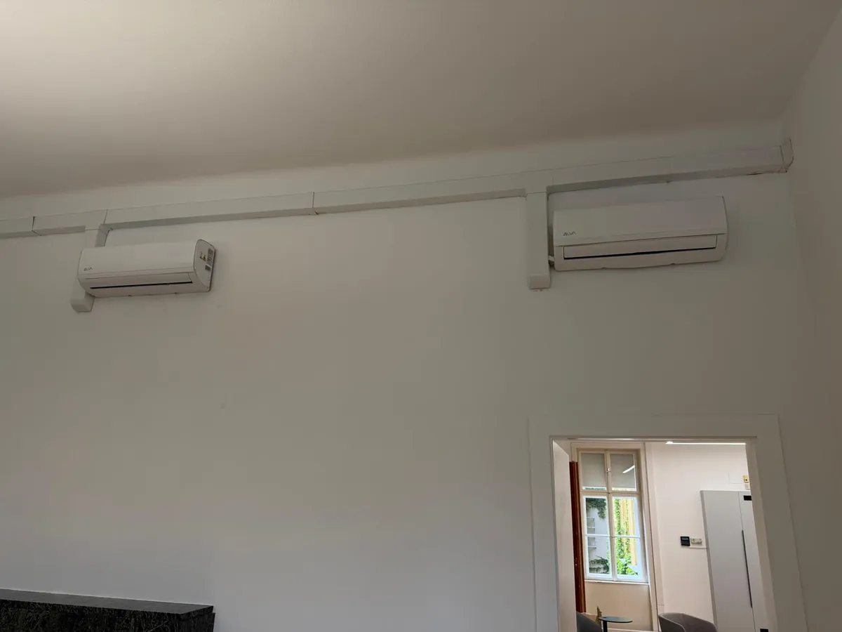 Zwei Split-Klimageräte an der Wand eines Büros in Wien, Leitungen in sauber verlegten Kanälen